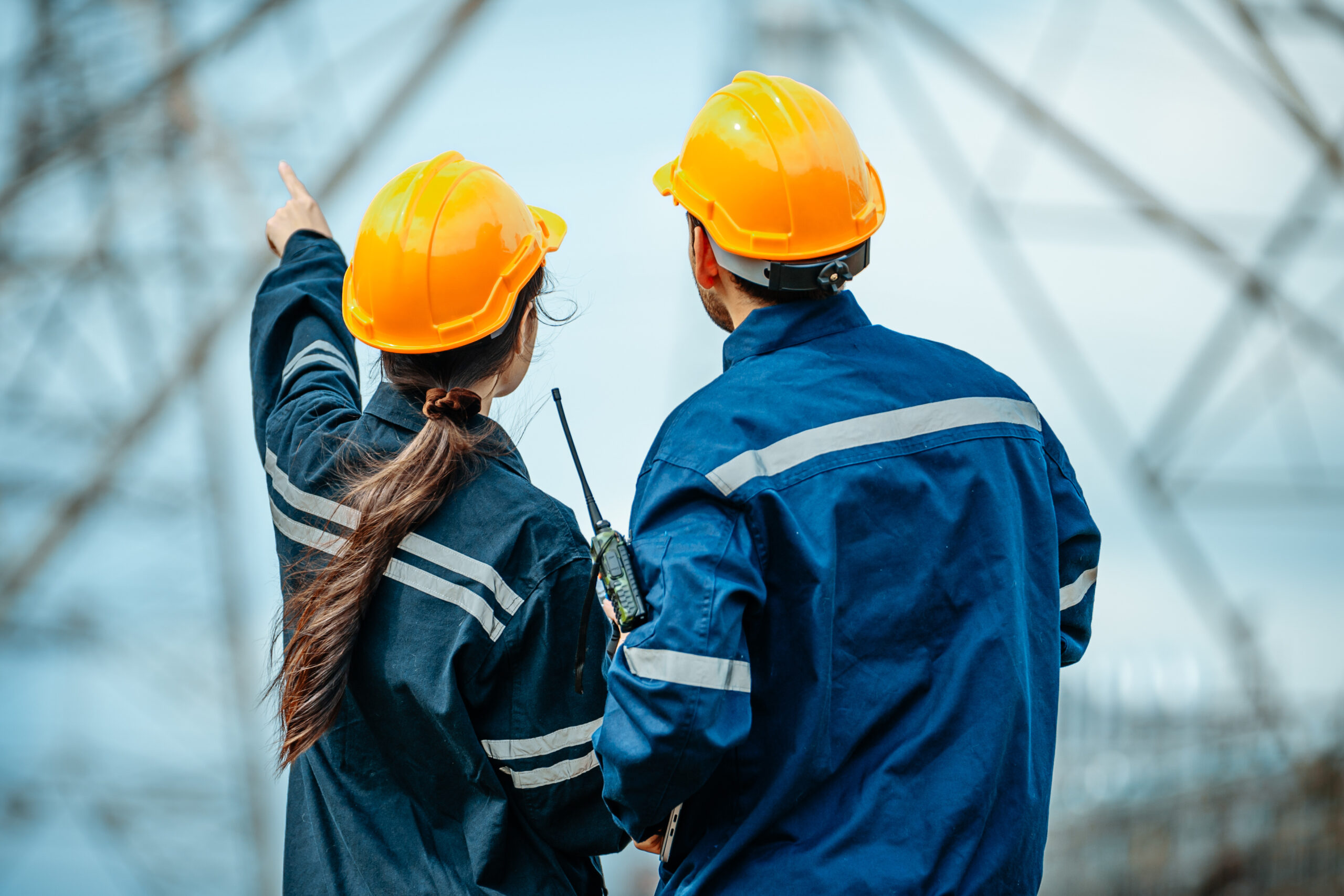 Workers examine and discuss power lines while wearing safety gear at an electrical substation during the day service-section-image-5