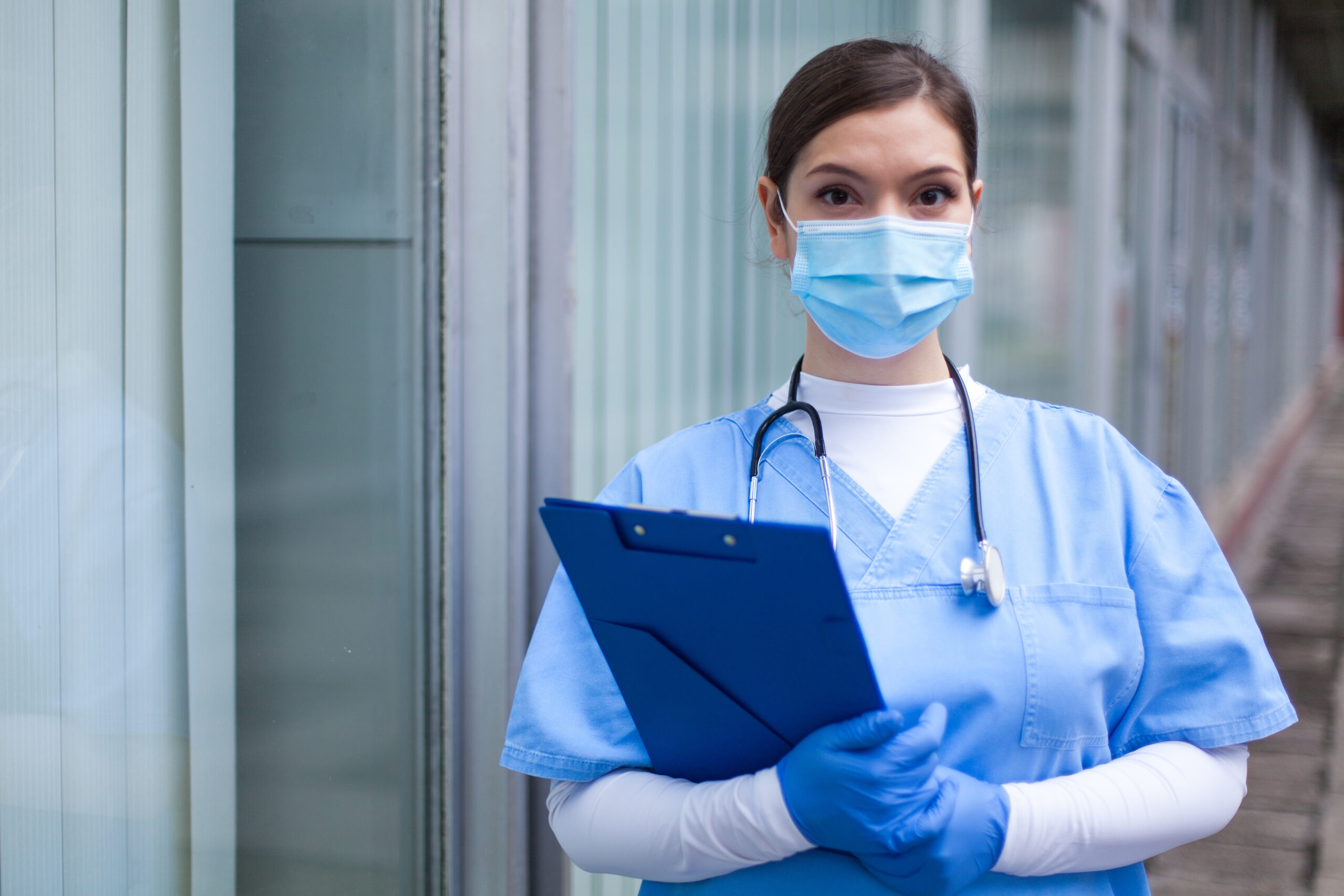 Female GP UK doctor holding blue clipboard standing outside hospital or clinic service-section-image-1