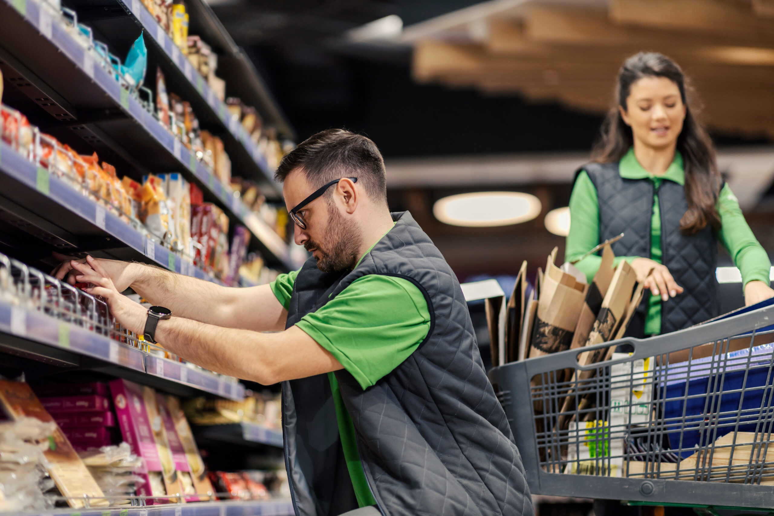 A supermarket worker is displaying groceries on shelves at marketplace. Divi-About-Us-Section-Hero-Image-2